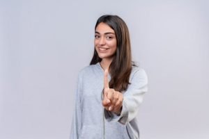 Una mujer joven señalando su dedo sobre un fondo gris. (conseguir prospectos)
