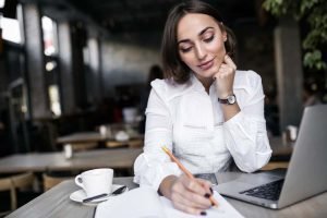 Una mujer sentada en una mesa con una computadora portátil y una taza de café en una página de destino.