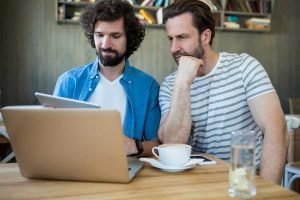 Dos hombres usan Google en una computadora portátil en una cafetería.