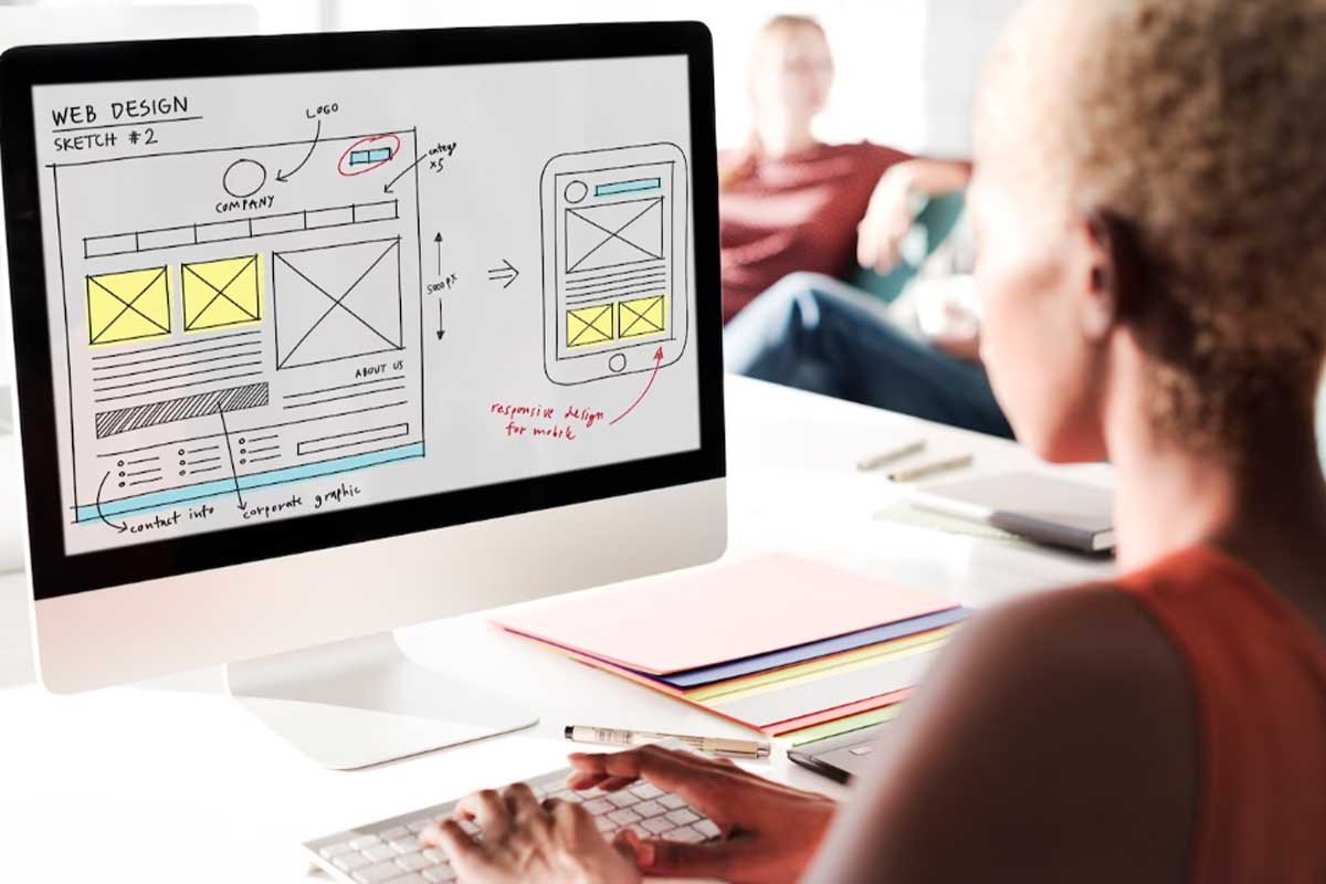 Una mujer diseñando una página web en la pantalla de su computadora.