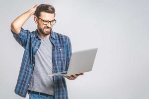 Un hombre con anteojos sostiene una computadora portátil y se mira el cabello, experimentando errores de segmentación en Facebook.